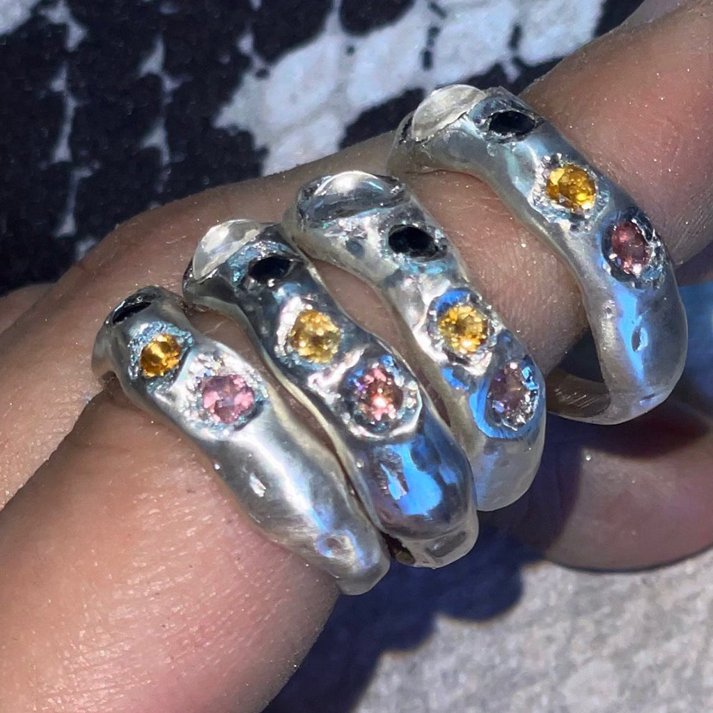 Silver rings with colorful gemstones on a finger against a patterned background