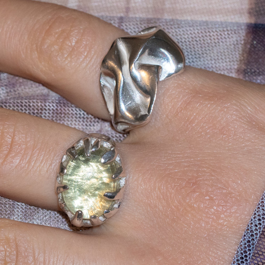 Silver ring with a yellow gemstone on a finger against a plaid fabric background