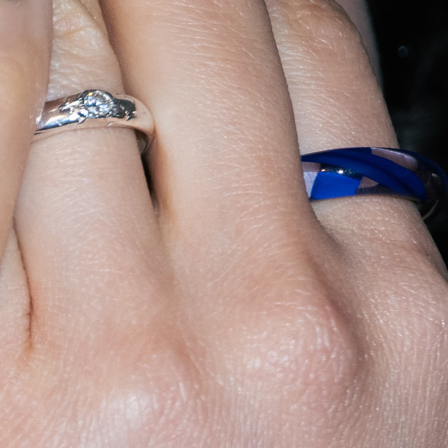 Close-up of a hand with two rings, one silver and one blue glass, on a blurred background.