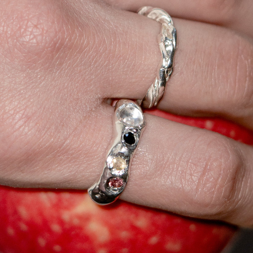 Silver ring with embedded stones on a finger against a red apple background