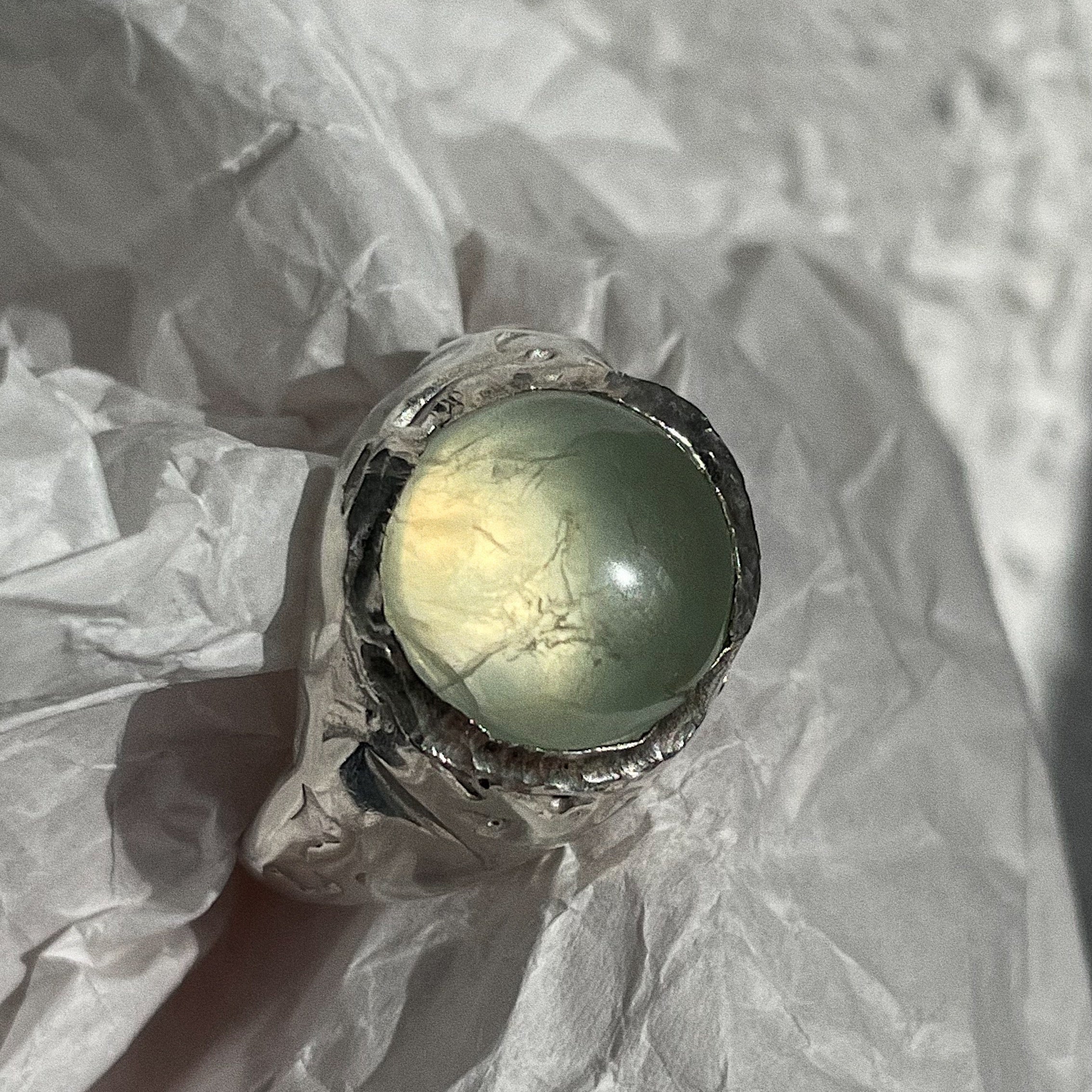 Silver ring with a green gemstone on crumpled paper
