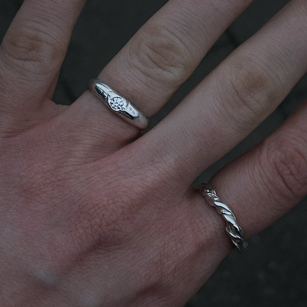 Hand wearing two silver rings from brand All Rivers, with a dark background