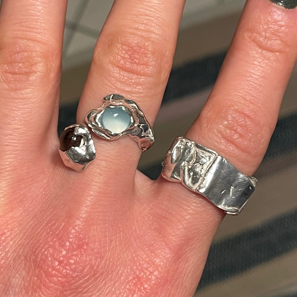 Hand wearing two silver rings with a textured band and a more polished design.