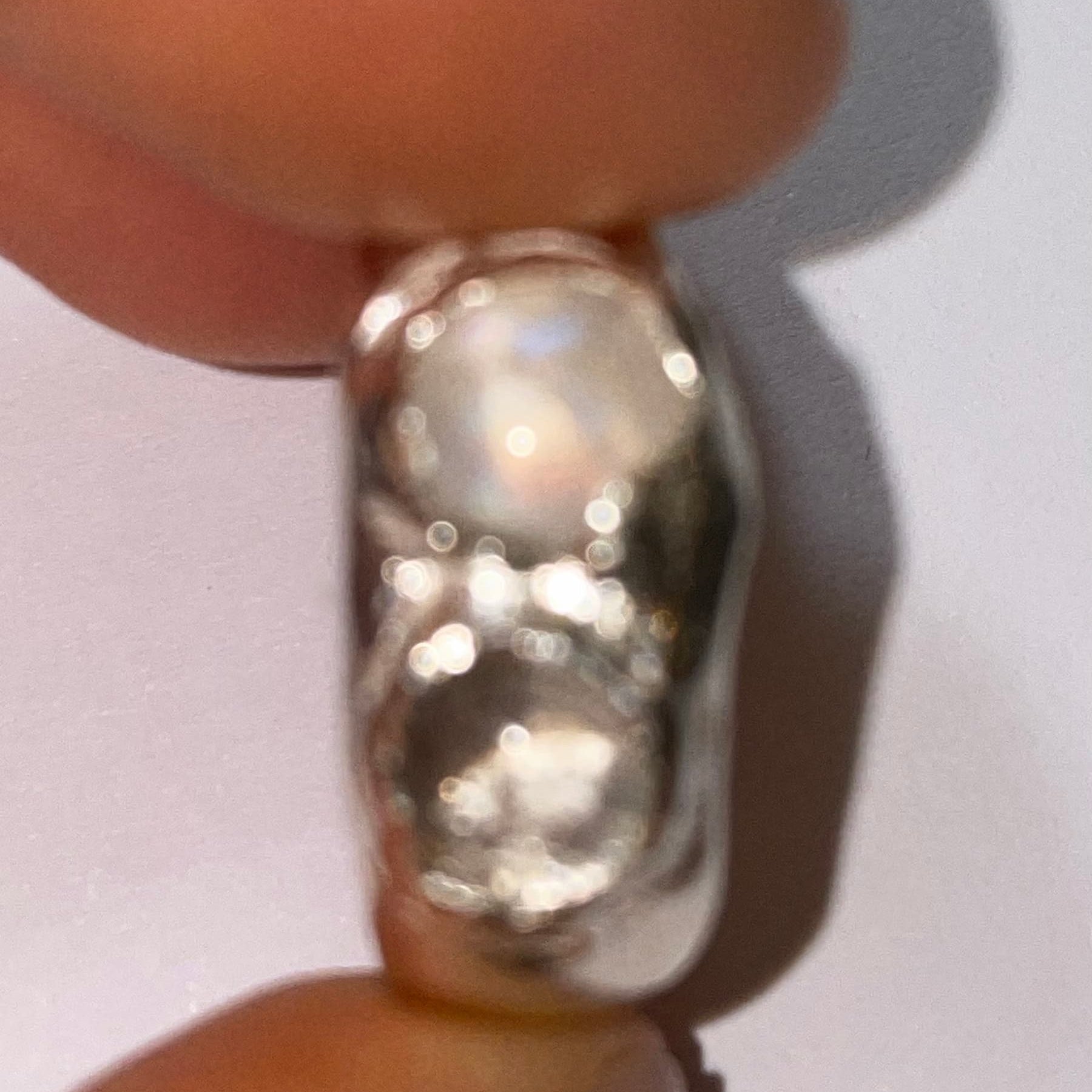 Silver ring held between two fingers on a light background