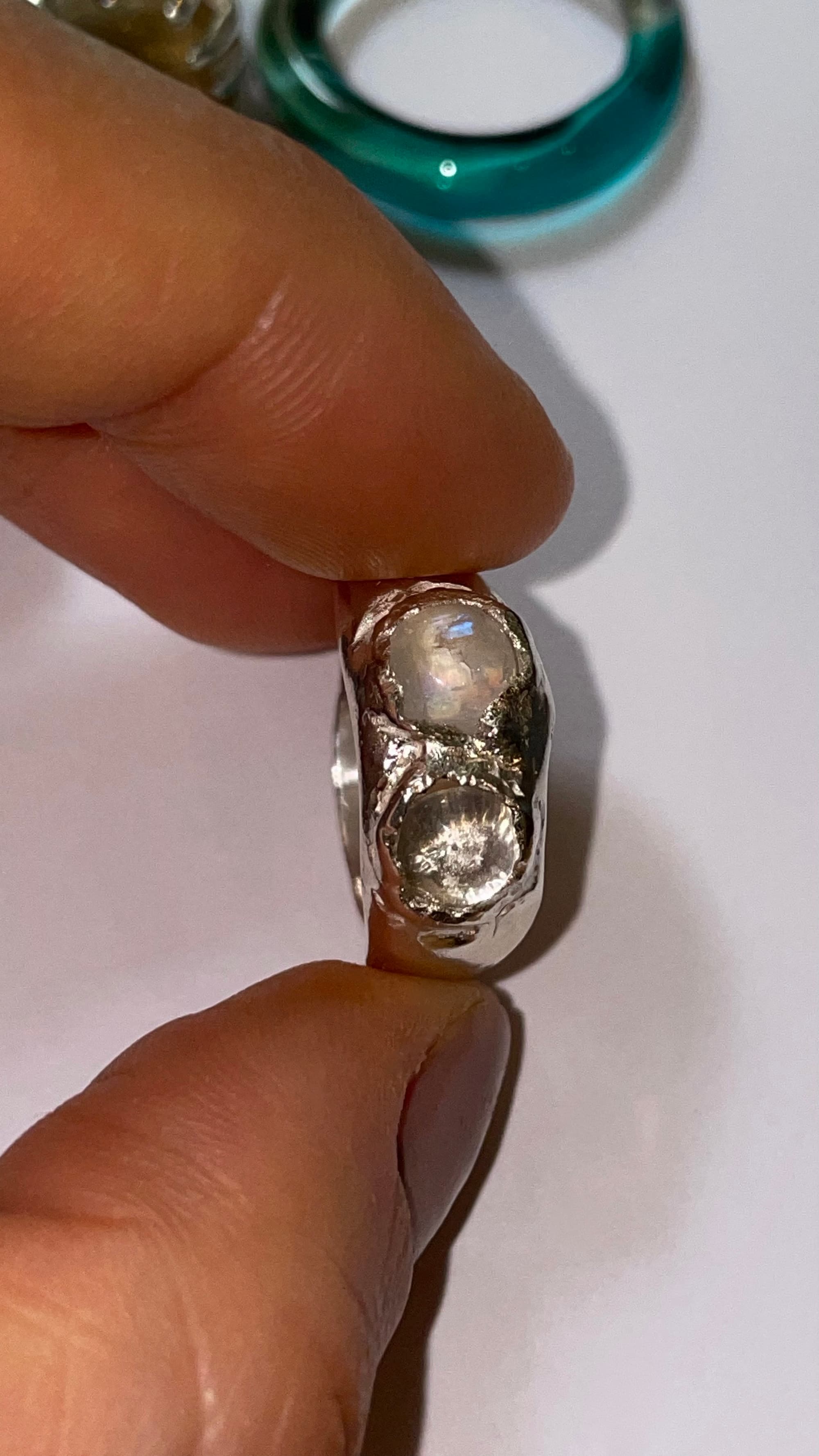 Silver ring with two large gemstones held between fingers on a white background